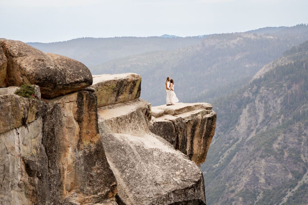 Couple standing together on a granite cliff overlooking Yosemite Valley during an adventurous Yosemite elopement.