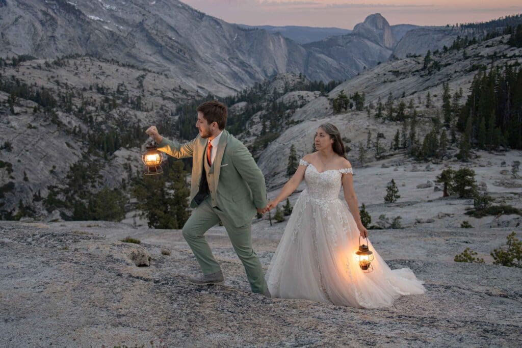 Newlywed couple holding hands and carrying glowing lanterns at sunset during a Yosemite elopement at Olmsted Point, with Half Dome visible in the background.