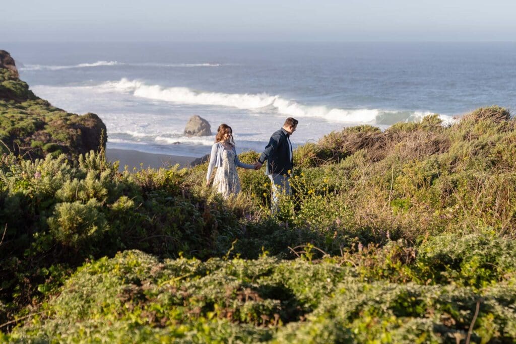 couple holding hands walking on a cliff in Big Sur